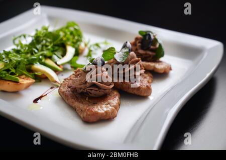 Nahaufnahme von köstlicher Bruschetta mit Salatrakete und Avocado auf weißem Teller im Restaurant. Drei kleine geröstete Rindersteaks mit Paste, bla dekoriert Stockfoto