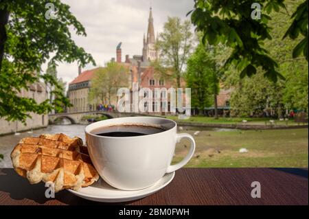 Kaffee mit belgischen Waffeln mit Blick auf Park, Kanal und historische Gebäude in Brügge, Belgien. Belgisches Frühstück. Stockfoto