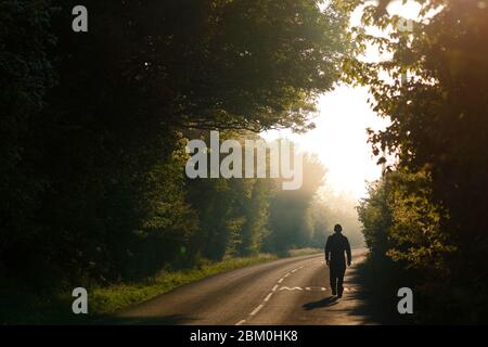 Ein Mann geht an einem nebligen Morgen im Fairburn ings Nature Reserve entlang einer Landstraße. Stockfoto