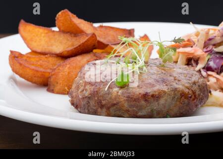 Ein Burger mit gebackenen Kartoffeln, Kohl und einem Salat in einem Keramikplatte auf einem Holztisch Stockfoto