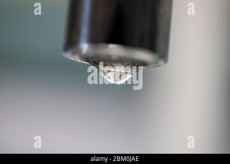 Ein Nahaufnahme eines Wassertropfens, der aus einem Wasserhahn tropft, mit einem unscharfen Hintergrund Stockfoto