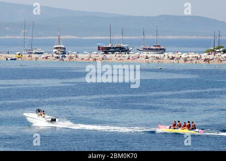 Ein Schnellboot, das Menschen auf einem bananenförmigen Schwimmer vor einem Sandstrand in Bol abschleppt Stockfoto