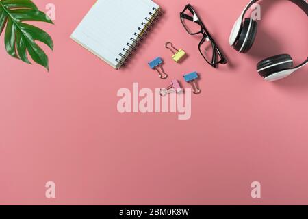 Draufsicht mit Brille, Notizbuch und Kopfhörer auf rosa Backgroup. Übersichtlichem Büroschreibtisch Hintergrund. Stockfoto