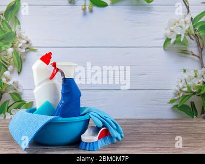Weiße Flasche, Spray, blauer Schwamm, Gummihandschuhe, Reinigungsset auf Frühlingshintergrund, pastellfarbene Holzplanken und Frühlingsblüten. Nahaufnahme. Frühling regelmäßig Stockfoto