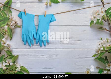 Gummihandschuhe, Reinigungsartikel auf Frühlingshintergrund, pastellfarbene Holzbohlen und Frühlingsblüten. Nahaufnahme. Frühling regelmäßige Reinigung. Flaches Lay. Leerer Platz Stockfoto