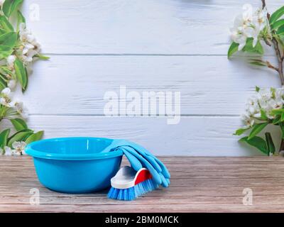Blaue Spülschale, Pinsel, blaue Gummihandschuhe, Reinigungsset auf Frühlingshintergrund, pastellfarbene Holzplanken und Frühlingsblüten. Nahaufnahme. Frühling regelmäßig Stockfoto