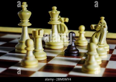 Schwarzer Bauer auf einem Schachbrett allein gegen alle weißen Figuren Stockfoto