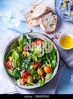 Frischer, farbenfroher Salat mit Kirschtomaten, Samen, Frühlingszwiebeln, Salatblättern mit einer Seite Sauerteig Brot Stockfoto