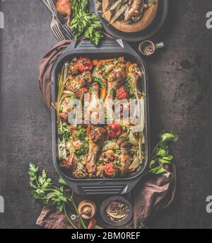 Ofen gebratenes Huhn und Gemüse in schwarzer Grill Bratpfanne mit Kräutern und Gewürzen auf rustikalem Hintergrund. Draufsicht Stockfoto