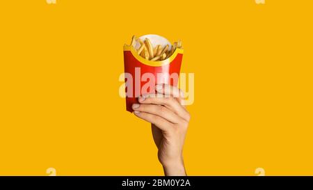 KHARKIV, UKRAINE - 4. APRIL 2020: Millennial guy zeigt kleine Packung pommes aus McDonald's auf orangefarbenem Hintergrund Stockfoto