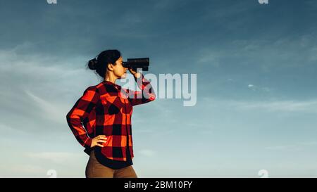 Attraktive Scout Mädchen schaut durch Fernglas auf blauen Himmel Hintergrund mit Copy-Space Stockfoto