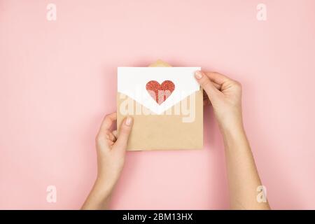 Liebesbrief in Frauenhand am Valentinstag. Handgefertigte Postkarte mit rotem Herz auf rosa Hintergrund. 14 Februar Konzept Stockfoto