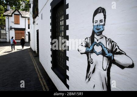 Die Menschen gehen an einem Kunstwerk des Künstlers vorbei, der als Rebellbär bekannt ist, nachdem es an einer Wand in der Ashton Lane in Glasgow erschien. Die neue Ergänzung zu Glasgows Street Art fängt die globale Coronavirus-Krise ein. Das Stück zeigt eine Krankenschwester, die eine Maske trägt und mit ihren Händen ein Liebesherz bildet, während Großbritannien weiterhin im Lockdown bleibt, um die Ausbreitung des Coronavirus zu verhindern. Stockfoto