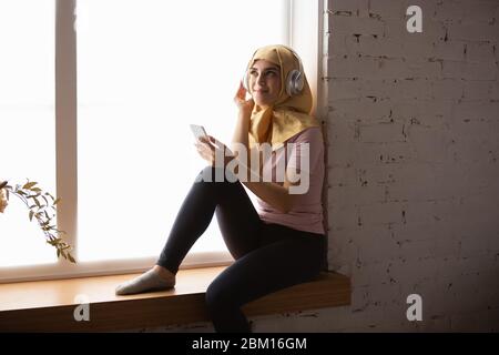 Eine hübsche junge muslimin zu Hause während der Quarantäne und Selbstisolierung. Arabisches weibliches Modell, das Zeit nützlich ist, isoliert zu sein. Konzept der Gesundheitsversorgung, Kommunikation, Bildung während der Pandemie. Stockfoto