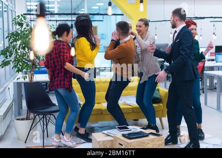 Young Business Team feiert einen guten Job im Büro. Gruppe junger Mitarbeiter tanzen im CO-Arbeitsbereich nach erfolgreicher Arbeit. Stockfoto