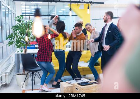 Young Business Team feiert einen guten Job im Büro. Gruppe junger Mitarbeiter tanzen im CO-Arbeitsbereich nach erfolgreicher Arbeit. Stockfoto