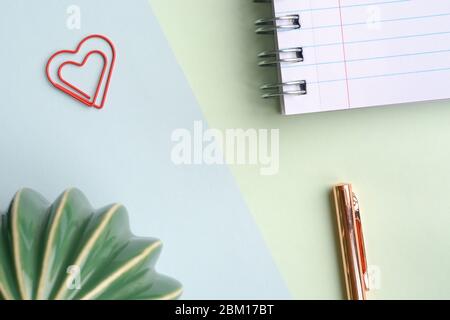 Pastellgrün blauer Hintergrund mit einem Notizbuch, Stift, Herz Büroklammer und Kaktus. Blick von oben, flach liegend. Stockfoto