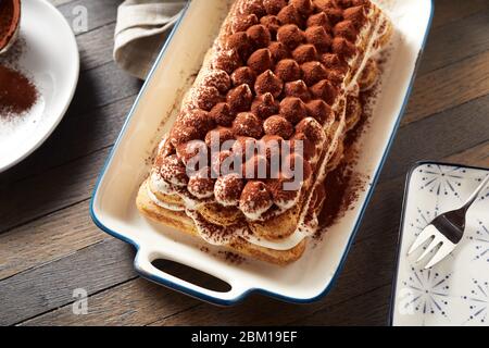 Draufsicht auf einem großen frisch zubereiteten italienischen Tiramisu auf einem rechteckigen Teller mit Kakaopulver bestreut serviert auf einem rustikalen Tisch Stockfoto