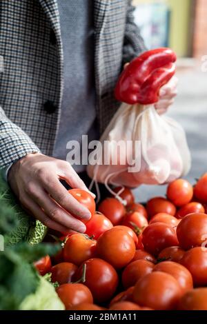 Nahaufnahme eines Mannes, der textile wiederverwendbare Netzbeutel verwendet, während er in einem Gemüsehändler einkauft, als Maßnahme zur Verringerung der Plastikverschmutzung Stockfoto
