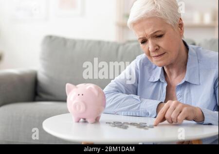 Keine Altersvorsorge. Verärgert ältere Frau Zählen Münzen aus Sparschwein Stockfoto