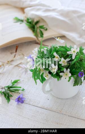 Helle Wochenendszene mit wilden Blumen in Tasse und einer Buchlesung Stockfoto