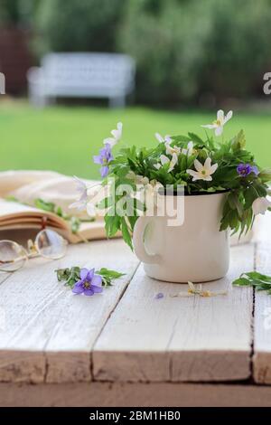 Weiße Anemonen aus Holz in einer Tasse auf einem Holztisch und einer weißen Gartenbank im Hintergrund gestylt Stockfoto