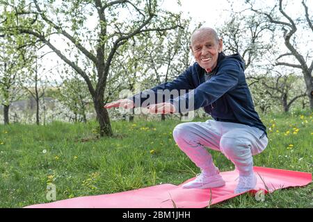 Großvater Rentner. Aktives Sport-Workout für alte Menschen. Sport und Altersvorsorge. Senior Mann auf rosa Yoga-Matte trainieren. Stockfoto