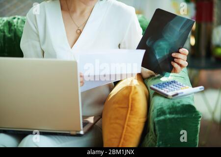 Nahaufnahme auf Frau in weißer Bluse mit Dokumenten und Taschenrechner Wahl der Krankenversicherung digital im Wohnzimmer an sonnigen Tag. Stockfoto