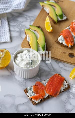 Frühstück am Morgen, zartes hausgemachtes Weichkäse auf Crackern mit geräucherter Forelle und Avocado Stockfoto