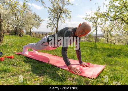 Gealterter gewöhnlicher Mann geht zu Hause Sport. Helles Bild von echten Trainingsanfängern stehen in Plankenposition auf einer Yogamatte. Stockfoto