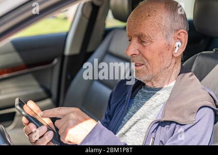 Fröhlicher, fröhlicher älterer Mann, der im Auto sitzt und sich für einen Ort entscheidet, an dem man telefonieren kann Stockfoto