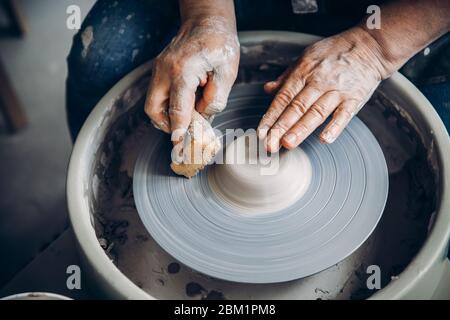 Faltige Hände Zauberer auf Töpferscheibe macht Tongeschirr. Ort zum Arbeiten. Stockfoto