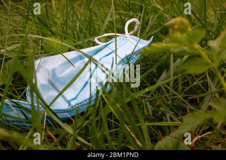 Gebrauchte chirurgische Maske auf dem Gras während der Covid-19 Pandemie gekippt. Weggeworfene Gesichtsmaske, die verwendet wird, um die Ausbreitung des Coronavirus zu schützen, der um Pose p liegt Stockfoto