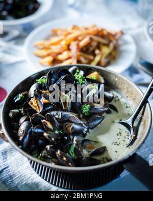 Moules Frites – Muscheln mit pommes Frites. Pommes Frites in einer schwarzen Pfanne mit pommes Frites im Hintergrund. Stockfoto