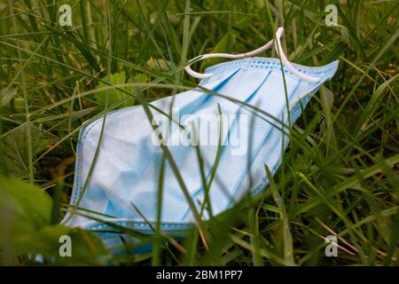 Gebrauchte chirurgische Maske auf dem Gras während der Covid-19 Pandemie gekippt. Weggeworfene Gesichtsmaske, die verwendet wird, um die Ausbreitung des Coronavirus zu schützen, der um Pose p liegt Stockfoto