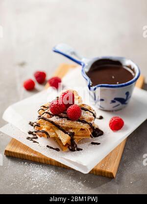 Süße Waffeln auf einem Tisch mit frischen Himbeeren und Schokolade dekoriert. Stockfoto