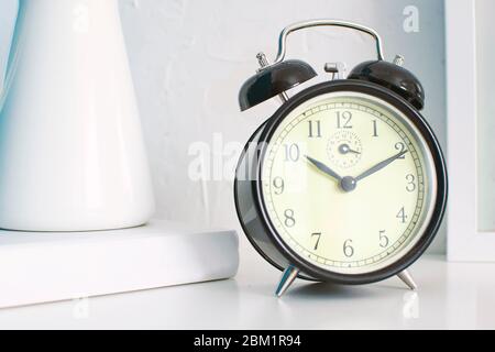 Nahaufnahme des Weckers in einem Schlafzimmer. Weißer Nachttisch aus Holz und leerer Platz für den Text des Editors. Stockfoto