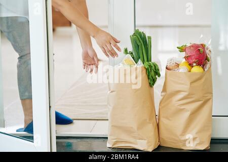 Frau, die Papiertaschen mit frischen Lebensmitteln, die sie online während der Sperrung bestellt Stockfoto