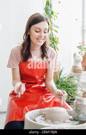 Töpferscheibe arbeiten. Glückliche junge Frau in roter Schürze Skulpturen aus Ton. Stockfoto