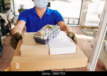 Lieferung Mann in medizinischen Maske und Handschuhe geben Pappkartons mit Pizza und Zahlungsterminal an den Kunden Stockfoto