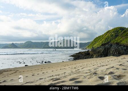 Atemberaubende Aussicht auf den Strand Selong Belanak, flankiert von einer grünen Bergküste. Selong Belanak Beach ist ein wunderschöner weißer Sandstrand in Lombok. Stockfoto