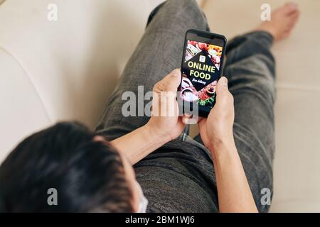 Nahaufnahme Bild des jungen Mannes ruht auf dem Sofa, Überprüfung Café-Anwendung und die Wahl, was online zum Abendessen bestellen Stockfoto