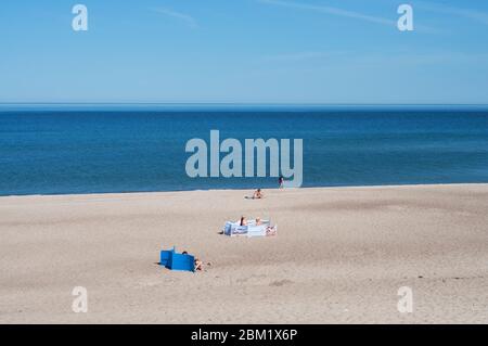 Ein paar Leute sonnen sich an einem leeren Strand auf Sonnenliegen voneinander entfernt an einem Sommertag am Meer Stockfoto