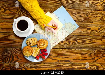 Leichtes Frühstück, frisches Gebäck und Kaffee, auf einem alten Holztisch. Touristisches Konzept. Reise-Blogger Frühstück Bau eines Routenplans mit einer Tasse Kaffee Stockfoto