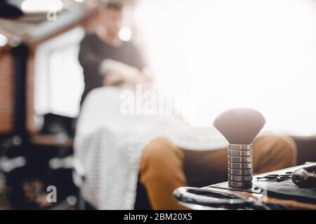 Bürste für Rasierbart zusammen mit Schüssel, verschwommener Hintergrund des Friseursalons für Männer, friseursalon Stockfoto