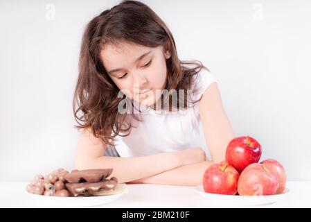 Kinder und Schokolade. Ein fröhliches Mädchen wählt zwischen Schokolade und Äpfeln. Gesunde Ernährung Stockfoto