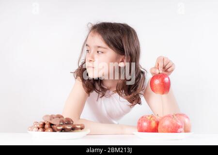 Kinder und Schokolade. Ein fröhliches Mädchen wählt zwischen Schokolade und Äpfeln. Gesunde Ernährung Stockfoto