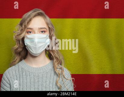 Junge Frau, die eine Gesichtsmaske mit Nationalflaggen Spanien trägt. Grippeepidemie und Virenschutzkonzept Stockfoto