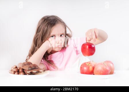 Kinder und Schokolade. Ein fröhliches Mädchen wählt zwischen Schokolade und Äpfeln. Gesunde Ernährung Stockfoto