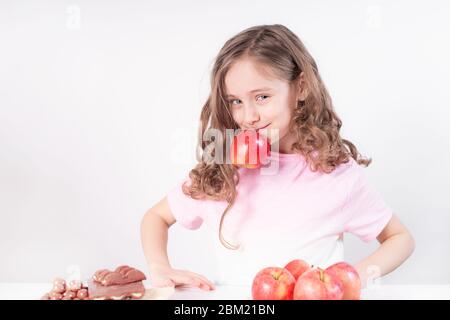 Kinder und Schokolade. Ein fröhliches Mädchen wählt zwischen Schokolade und Äpfeln. Gesunde Ernährung Stockfoto